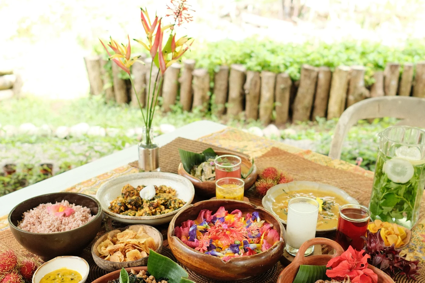 A long table set with bowls of fresh farm food and a tall arrangement of garden flowers, waiting in the green